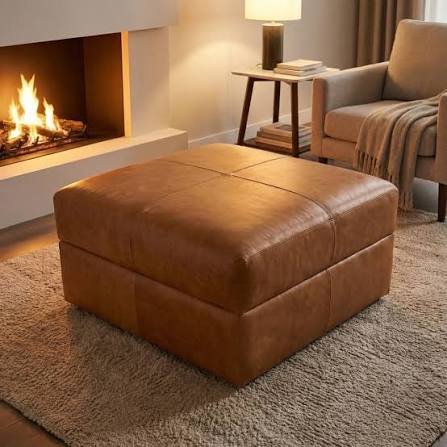 Square cognac leather ottoman beside a fireplace