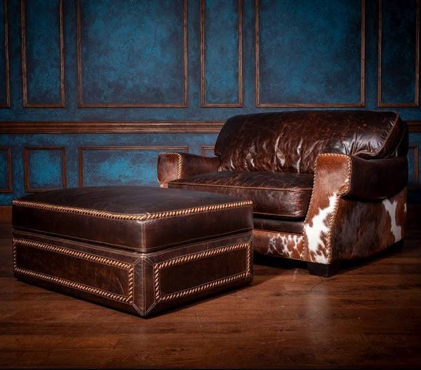 Dark leather ottoman with rope-stitch trim beside a matching cowhide chair